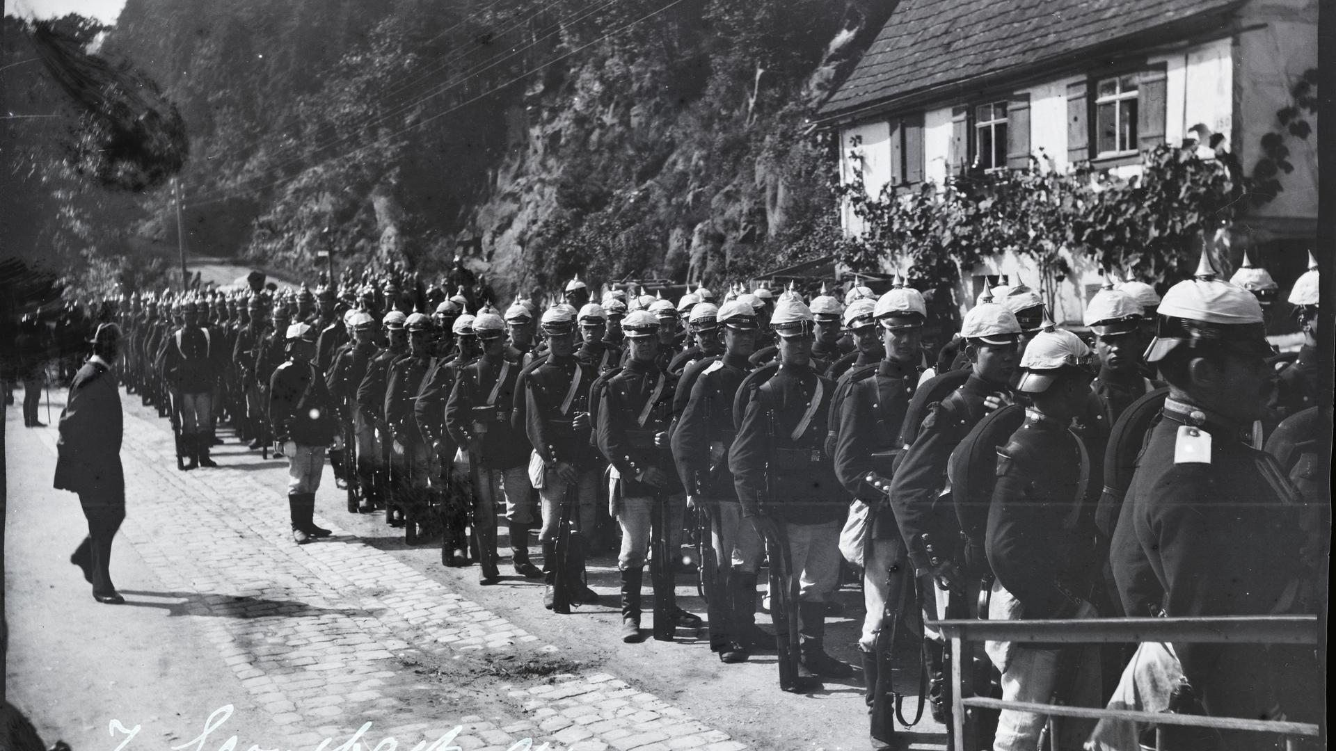 historische Aufnahme aus Gernsbach, eine große Anzahl Soldaten mit Pickelhauben marschiert eine Straße entlang