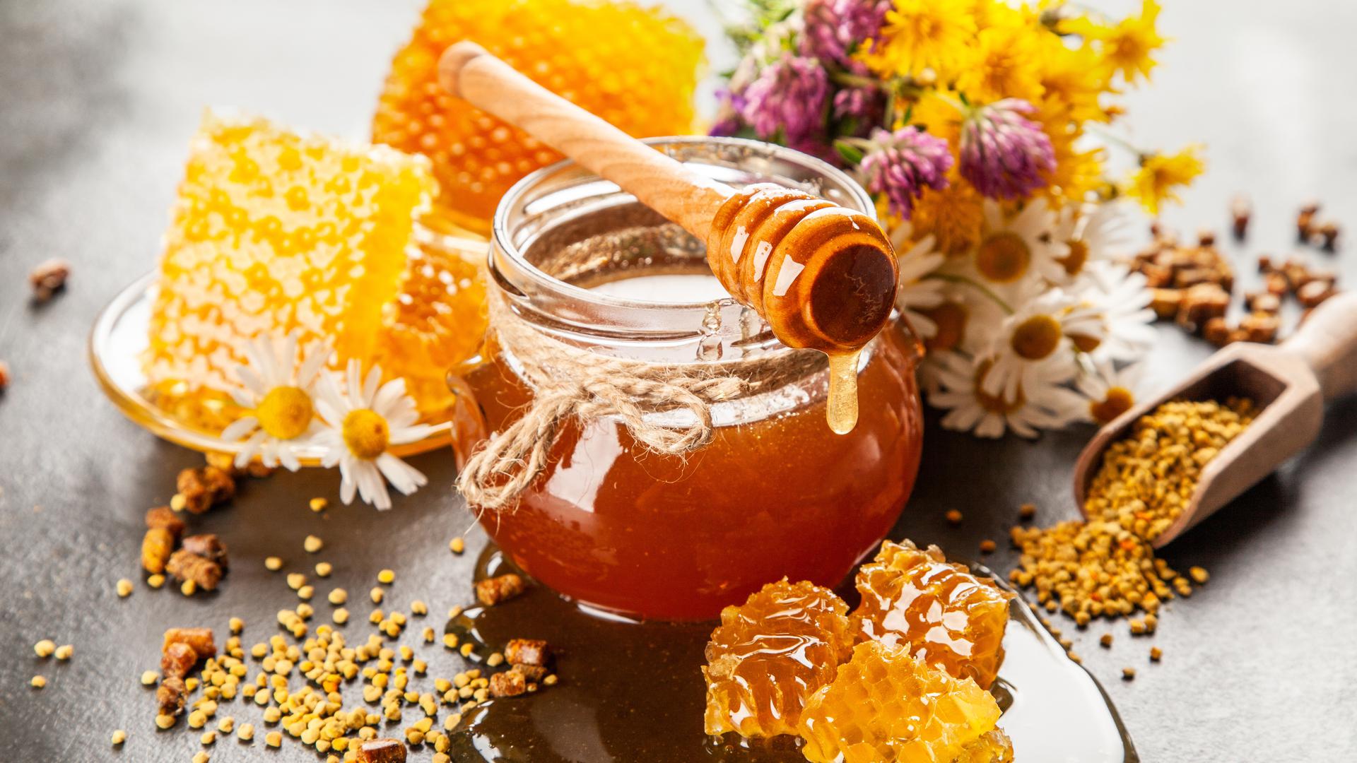Ein Glas Honig und Bienenwaben stehen auf einem Tisch. 