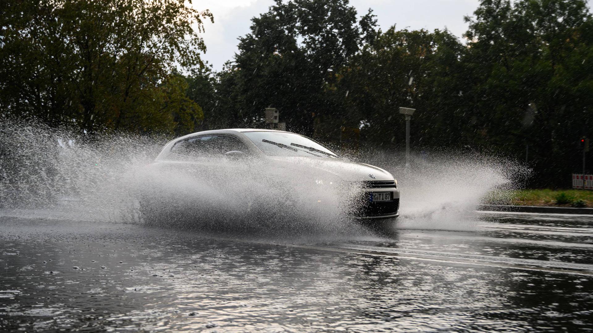 Ein Auto fährt bei starkem Regen durch eine überschwemmte Straße in Hannover.