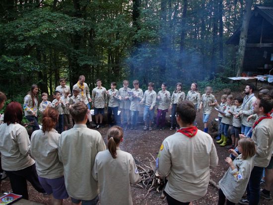 Kinder, Jugendliche und Betreuer stehen im Wald um ein Lagerfeuer.