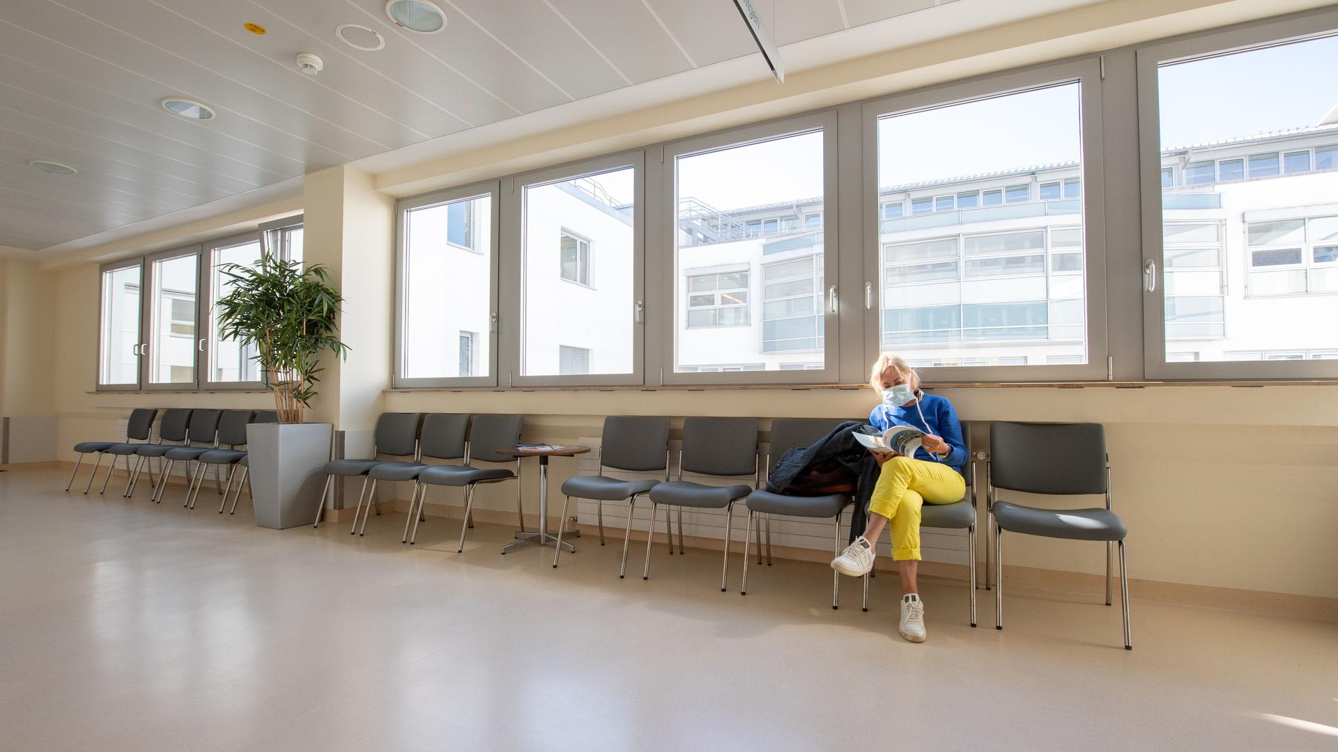 Eine Patientin mit Mundschutz wartet in einem ansonsten leeren Wartebereich.