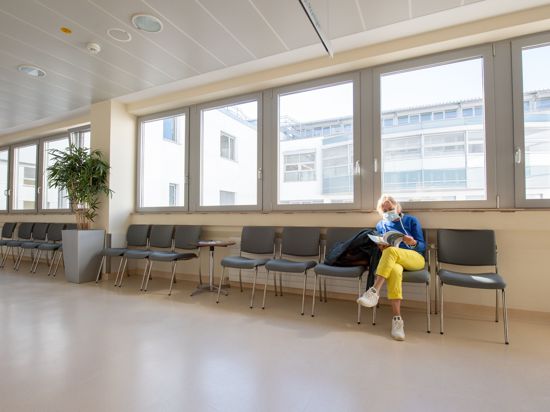 Eine Patientin mit Mundschutz wartet in einem ansonsten leeren Wartebereich.