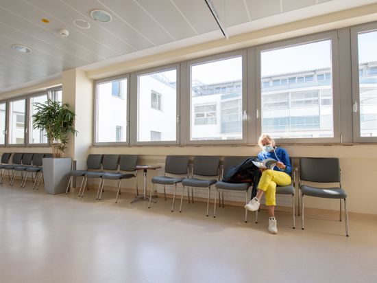 Eine Patientin mit Mundschutz wartet in einem ansonsten leeren Wartebereich