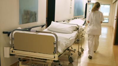 ARCHIV - Ein Krankenschwester eilt auf einem Flur an einem leeren Bett vorbei.