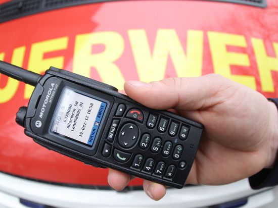 Ein Feuerwehrmann hält ein digitales Handfunkgerät vor seinem Fahrzeug.