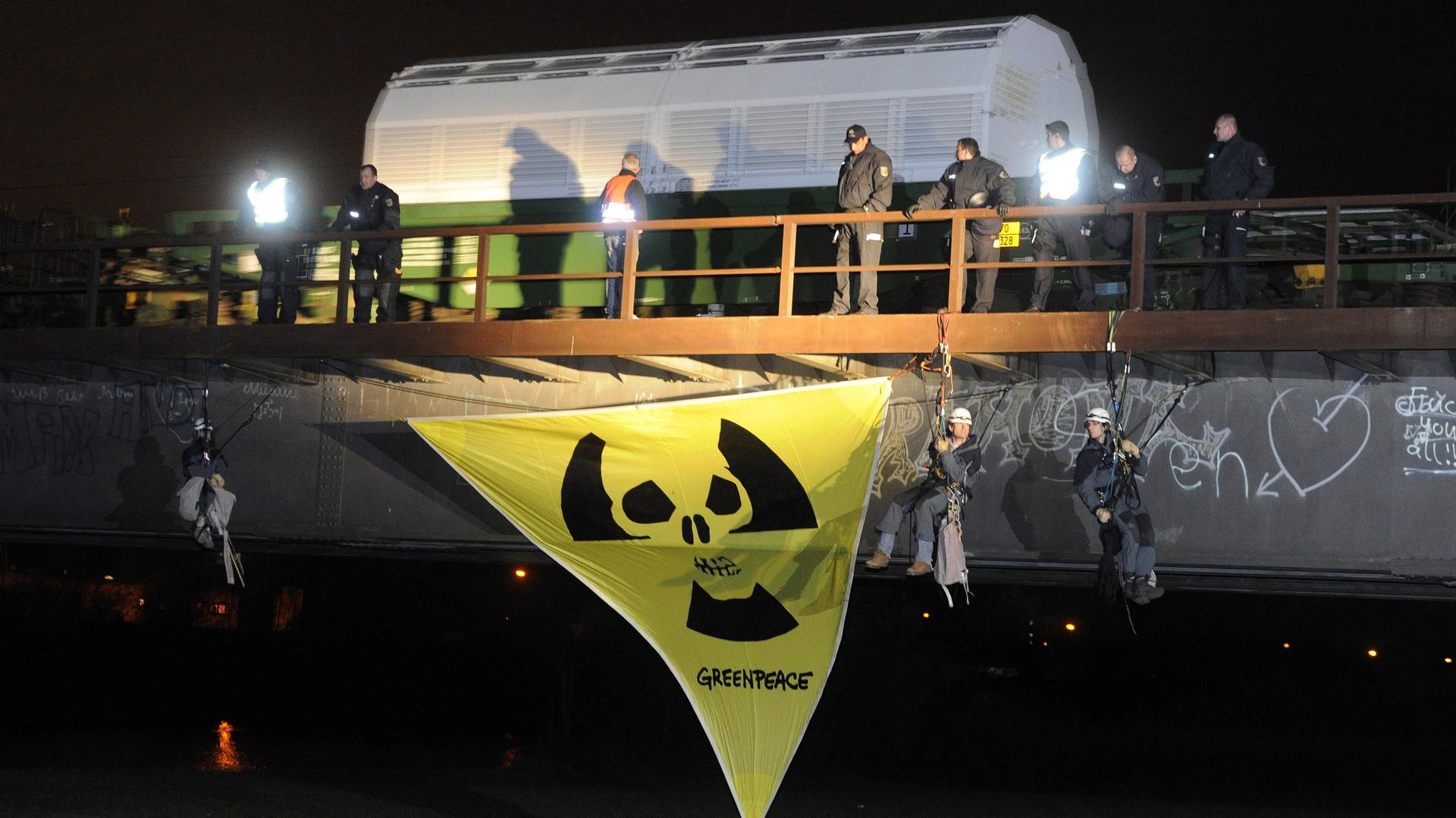 Ein Zug mit 11 Castor-Behältern fährt am Samstag (06.11.2010) aus dem Bahnhof des badischen Kehl. Unter der Brücke, über die er rollt, hängen Greenpeace Aktivisten, die gegen den Transport mit einem Transparent demonstrieren. Der Zug kommt aus der französischen Wiederaufbereitungsanlage La Hague und fährt nach Dannenberg . Er enthält 123 Tonnen Atommüll aus deutschen Kernkraftwerken. Foto: Uli Deck dpa/lrs +++(c) dpa - Bildfunk+++
