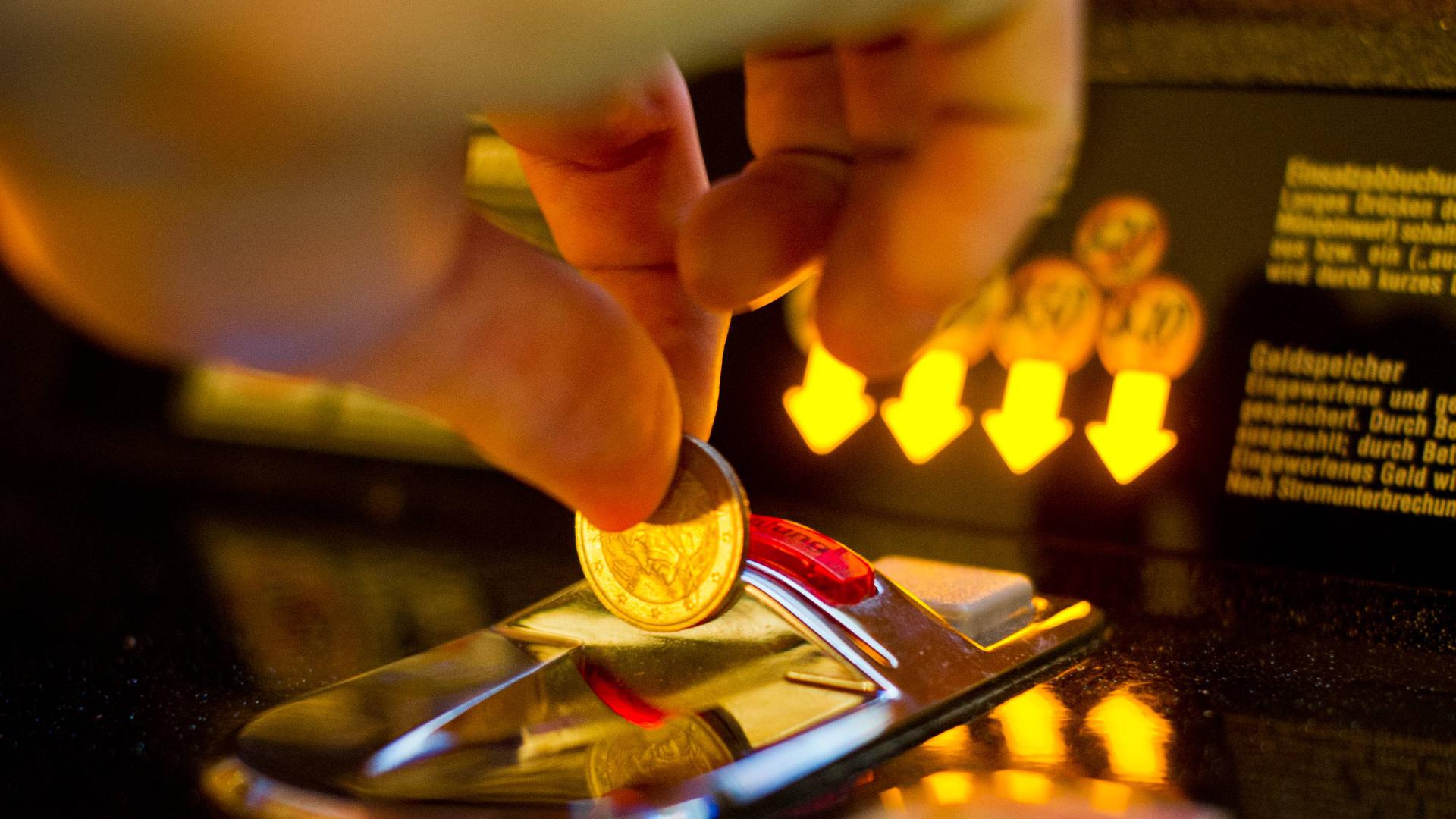 Eine Hand wirft eine Geldmünze in einen Spielautomaten.