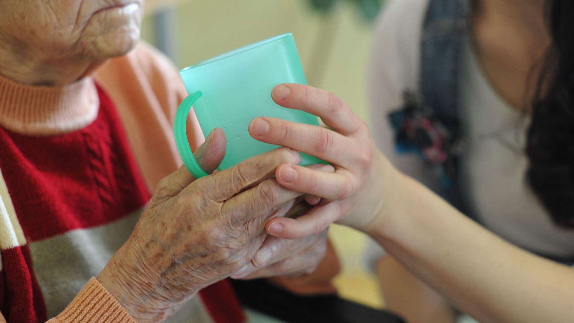 Eine Pflegekraft hilft einer alten Frau beim Trinken aus einem Becher in einem Seniorenheim.