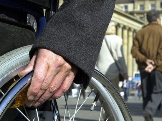 Die Hand eines Rollstuhlfahrers liegt auf dem Rad des Stuhls