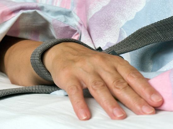 Eine mit einem Textilband festgebundene Hand eines Patienten - die Fixierung bzw. Fixation eines Patienten in der Krankenpflege durch Festschnallen am Handgelenk. 