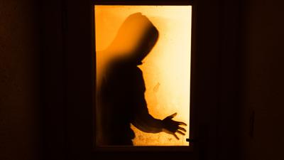 Der Schatten eines Mannes ist hinter einer gläsernen Wohnungstür zu sehen.