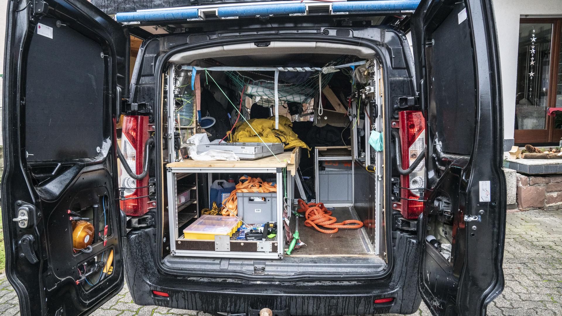 Auto mit geöffneten Hintertüren. Blick ins Innere: Rettungsseile, Werkzeug, Kisten, auf dem Dach ein Dachzelt