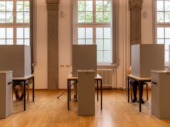 Bürger sitzen im Wahllokal für die Briefwahl in Wahlkabinen.