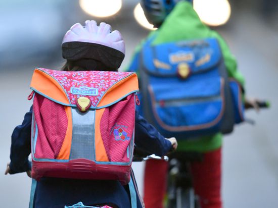 Kinder mit Fahrradhelmen radeln zur Schule. 