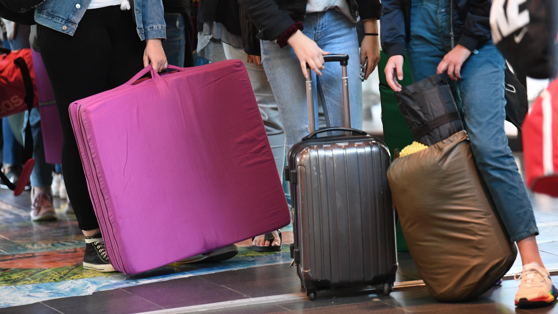 Jugendliche stehen mit Koffer, Isomatten, Schlafsack und Matratze da