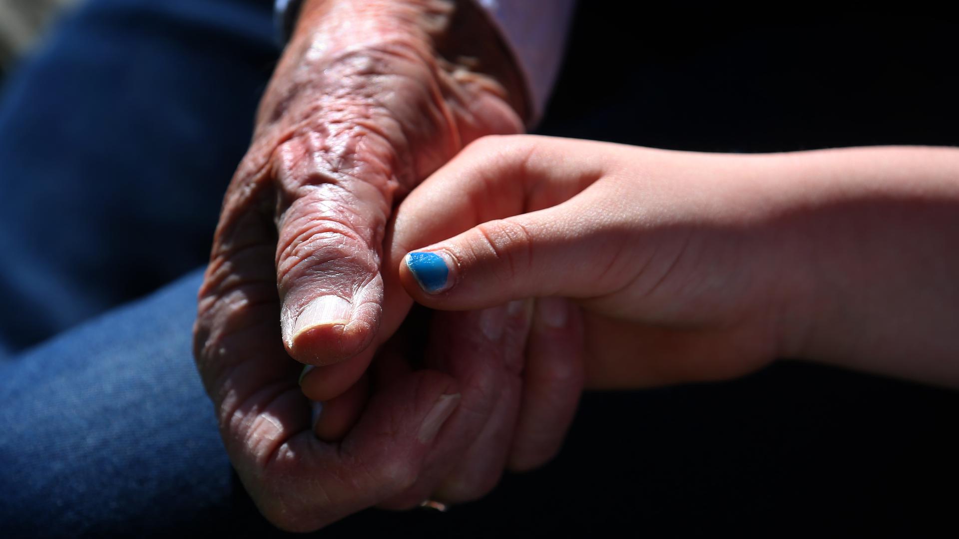 Eine 90-jährige Frau hält bei einem Verwandtenbesuch die Hand ihrer siebenjährigen Urenkelin. 