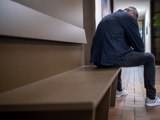 Ein Mann sitzt gebeugt auf einer Wartebank in einer Behörde.