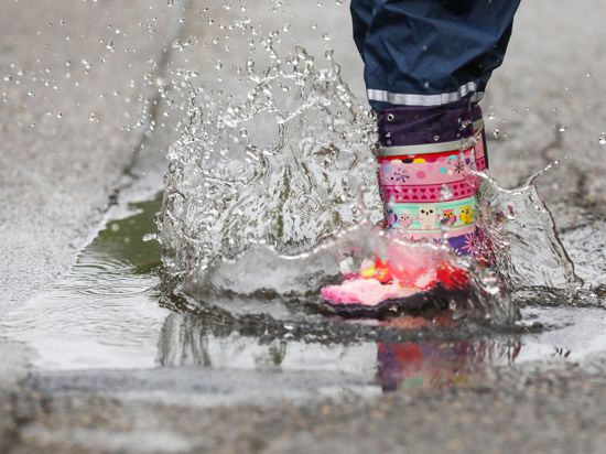 Ein Mädchen springt mit Gummistiefeln in eine Regenpfütze. 