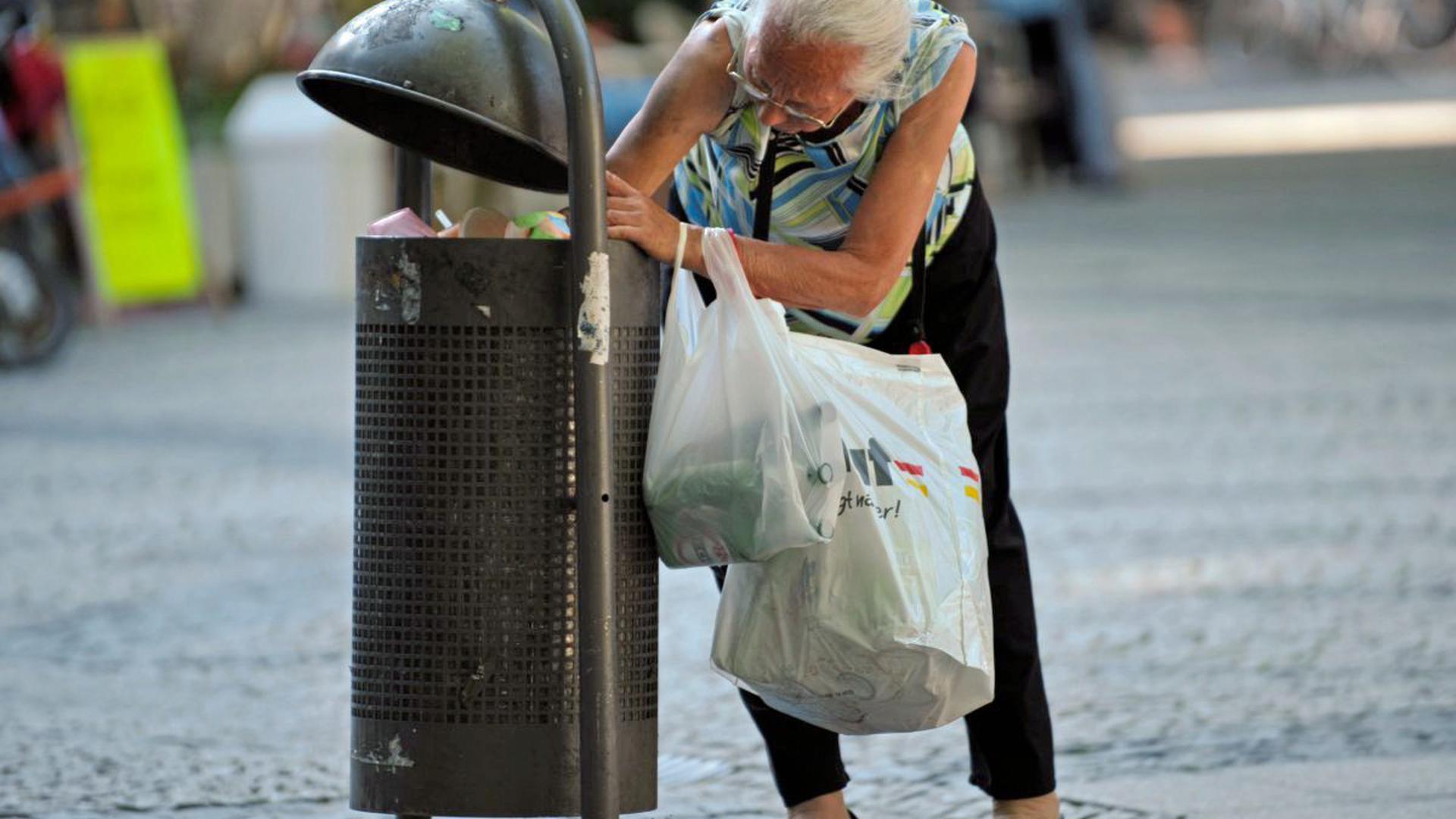 Eine alte Frau sucht in einer Mülltonne nach Pfandflaschen.