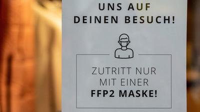 Ein Schild mit der Aufschrift "Zutritt nur mit einer FFP2 Maske!" ist an einem Eingang zu einem Bekleidungsgeschäft in der Innenstadt zu sehen.