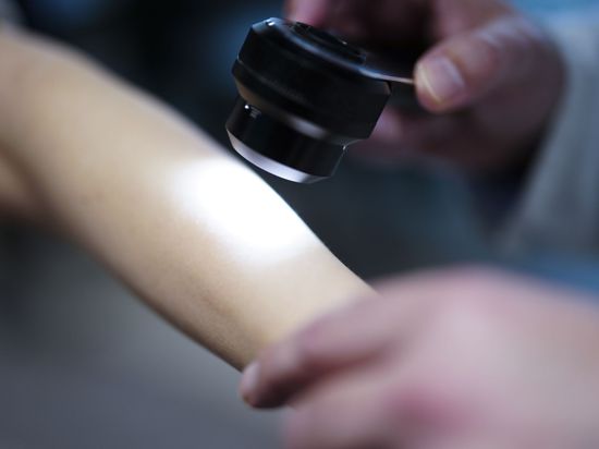ARCHIV - Ein Hautarzt untersucht bei einer Krebsvorsorgeuntersuchung eine Patientin mit einem Auflichtmikroskop. 