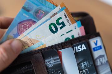 Eine Person hält eine Geldbörse mit zahlreichen Banknoten und Bankkarten in der Hand (gestellte Szene). 