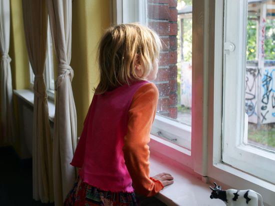 Ein kleines Mädchen schaut nachdenklich aus einem Fenster.