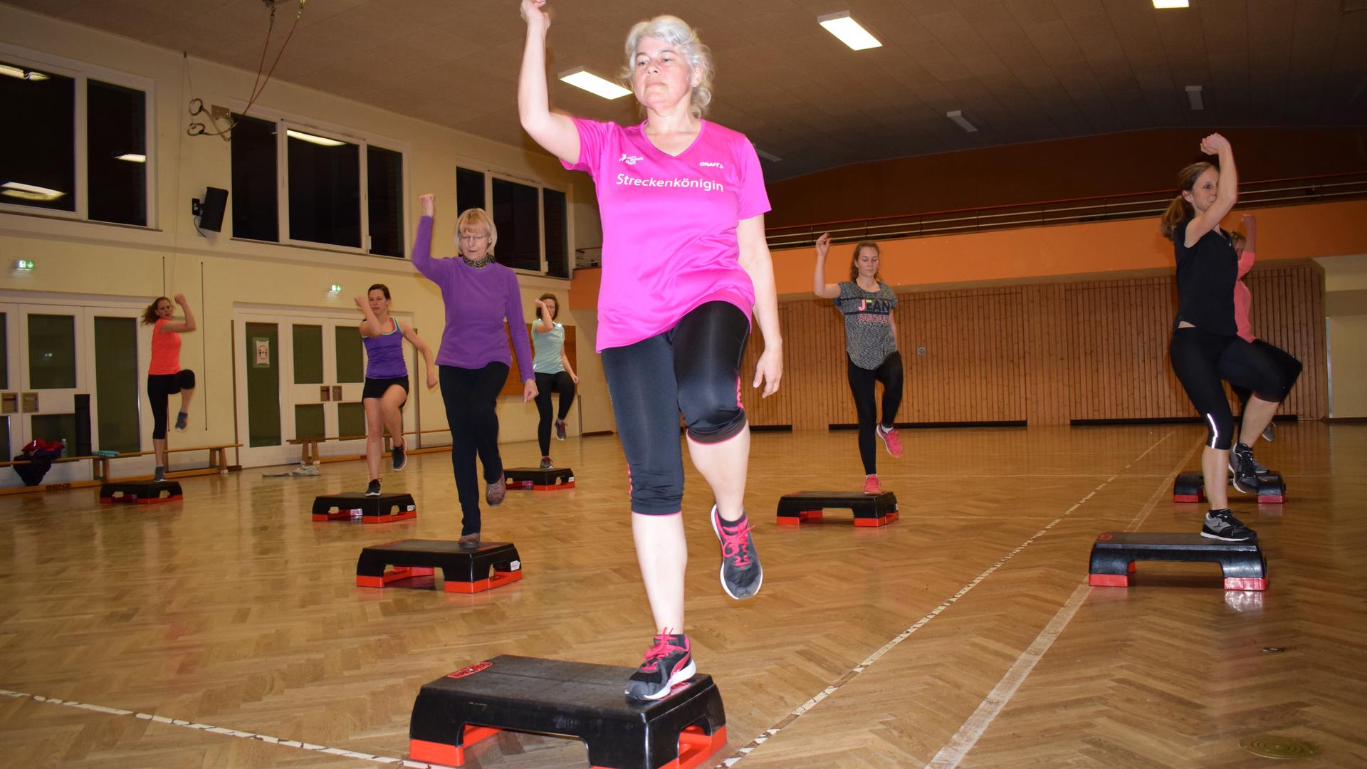 Several women do exercises on a stepper in a gym.