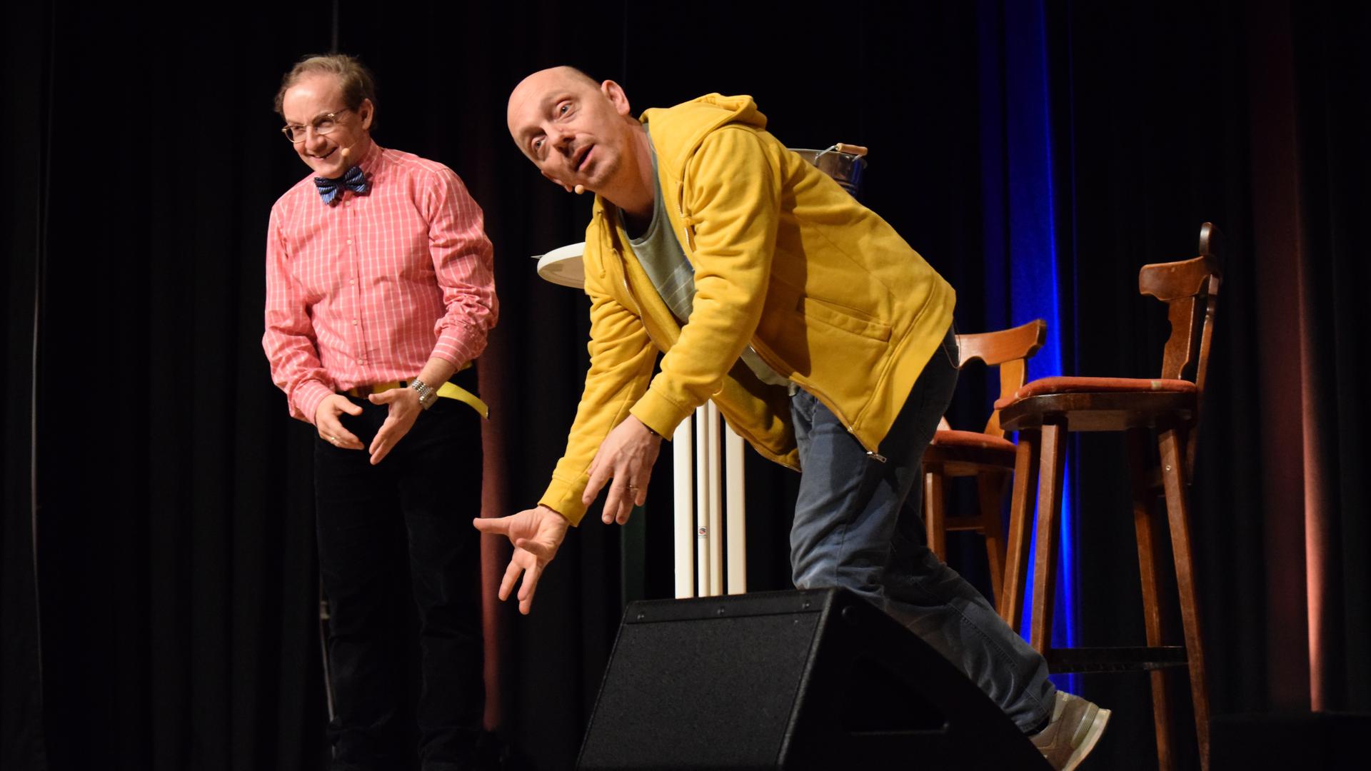 Zwei Comedians stehen auf einer Bühne und gestikulieren.