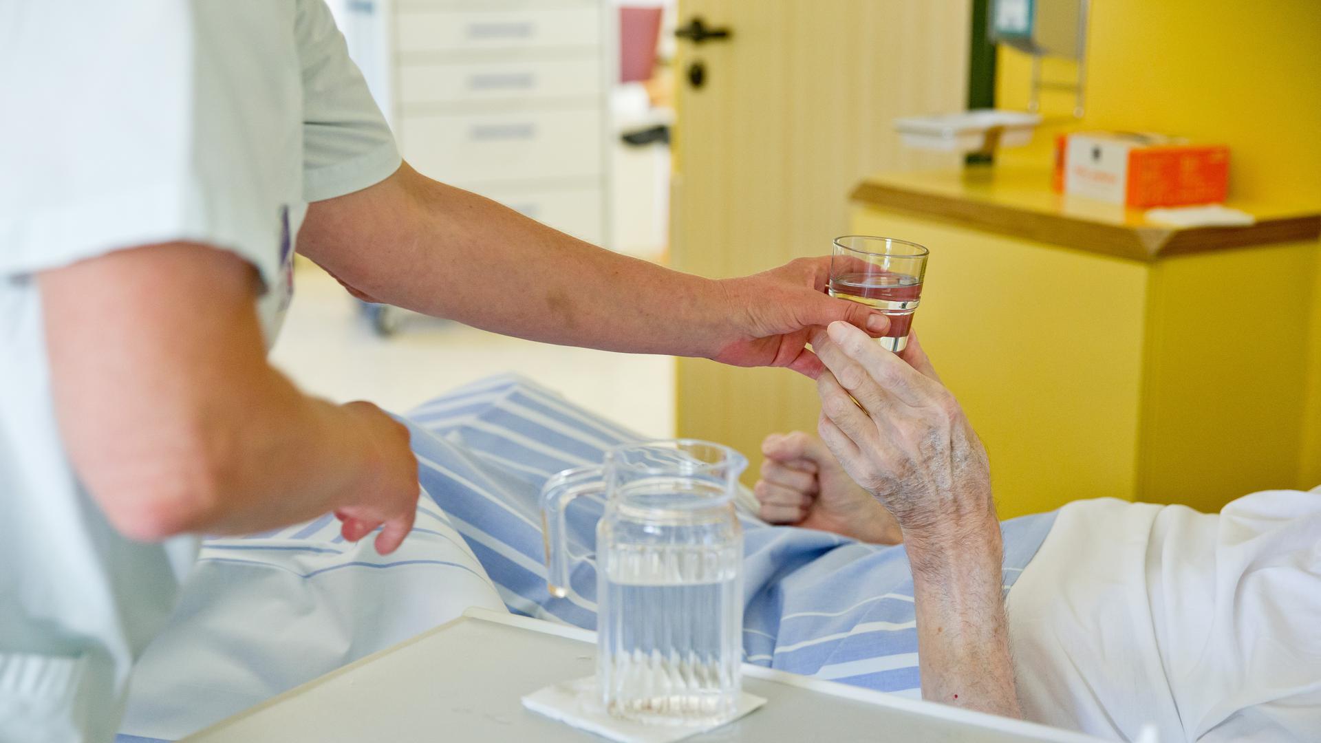 Eine Krankenpflegerin reicht einem Patienten in einem Klinikum ein Glas Wasser. 