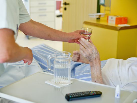 Eine Krankenpflegerin reicht einem Patienten in einem Klinikum ein Glas Wasser. 