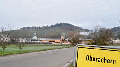 Eine Straße mit dem Ortsschild „Oberachern“ führt zu einer Fabrikanlage vor dem Hintergrund des Bienenbuckels.
