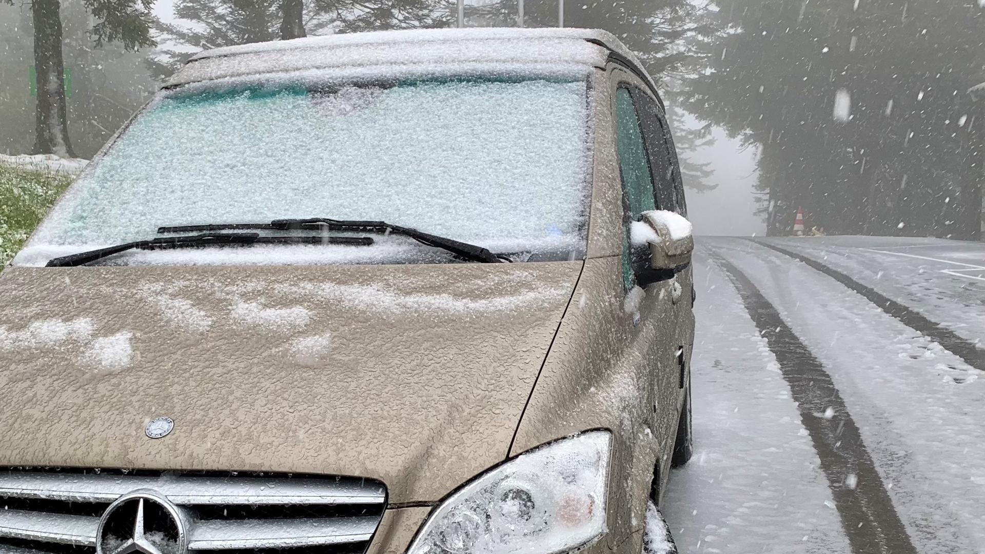 Ein parkendes Auto mit Schnee auf der Windschutzscheibe. Auch auf der Straße liegt eine dünne Schneeschicht.