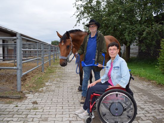 Ein Mann mit Cowboyhut und eine Frau im Rollstuhl neben einem braunen Pferd