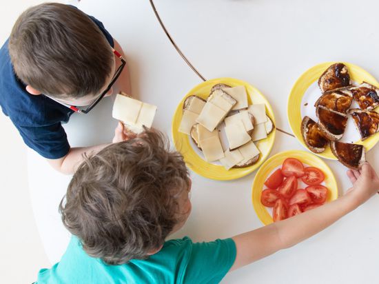 Zwei Kinder sitzen zum Frühstück in einem Kindergarten am Tisch und essen gemeinsam.