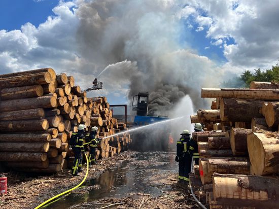 Feuerwehrleute löschen einen Brand zwischen Holzstapeln.