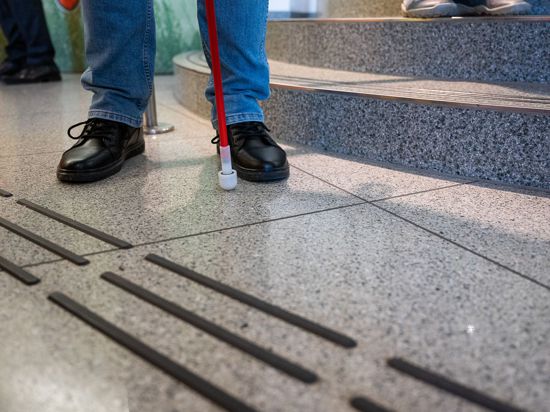 Eine blinde Person steht mit Langstock vor einem neu angebrachten Bodenleitsystem in einem Museum. Foto: Paul Glaser/dpa/Symbolbild