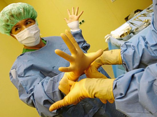 Eine Ärztin in einer Klinik bekommt OP-Handschuhe angezogen.