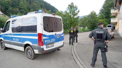 Polizisten stehen bei Oppenau vor einer Einfahrt in ein Waldgebiet.