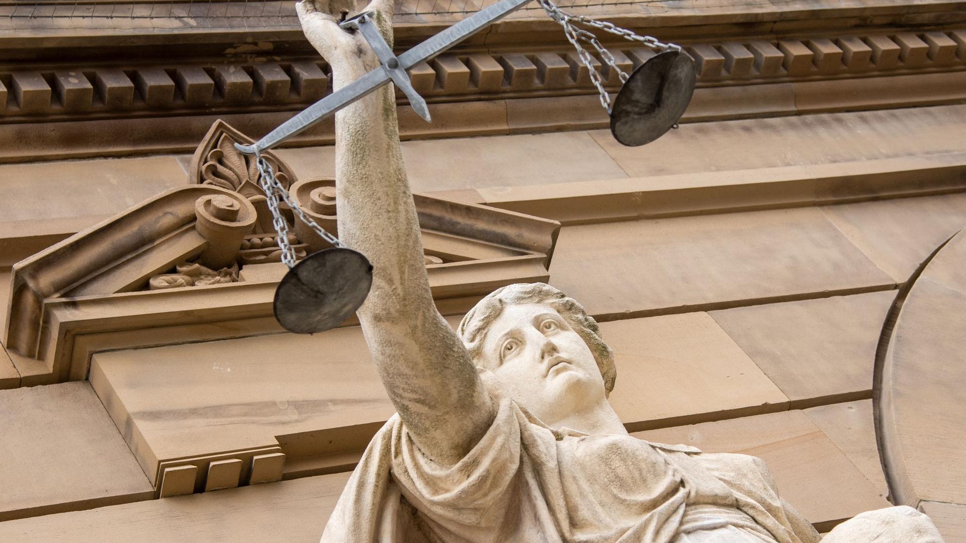 Vor einem Gericht hält eine Statue der Justitia eine Waagschale.