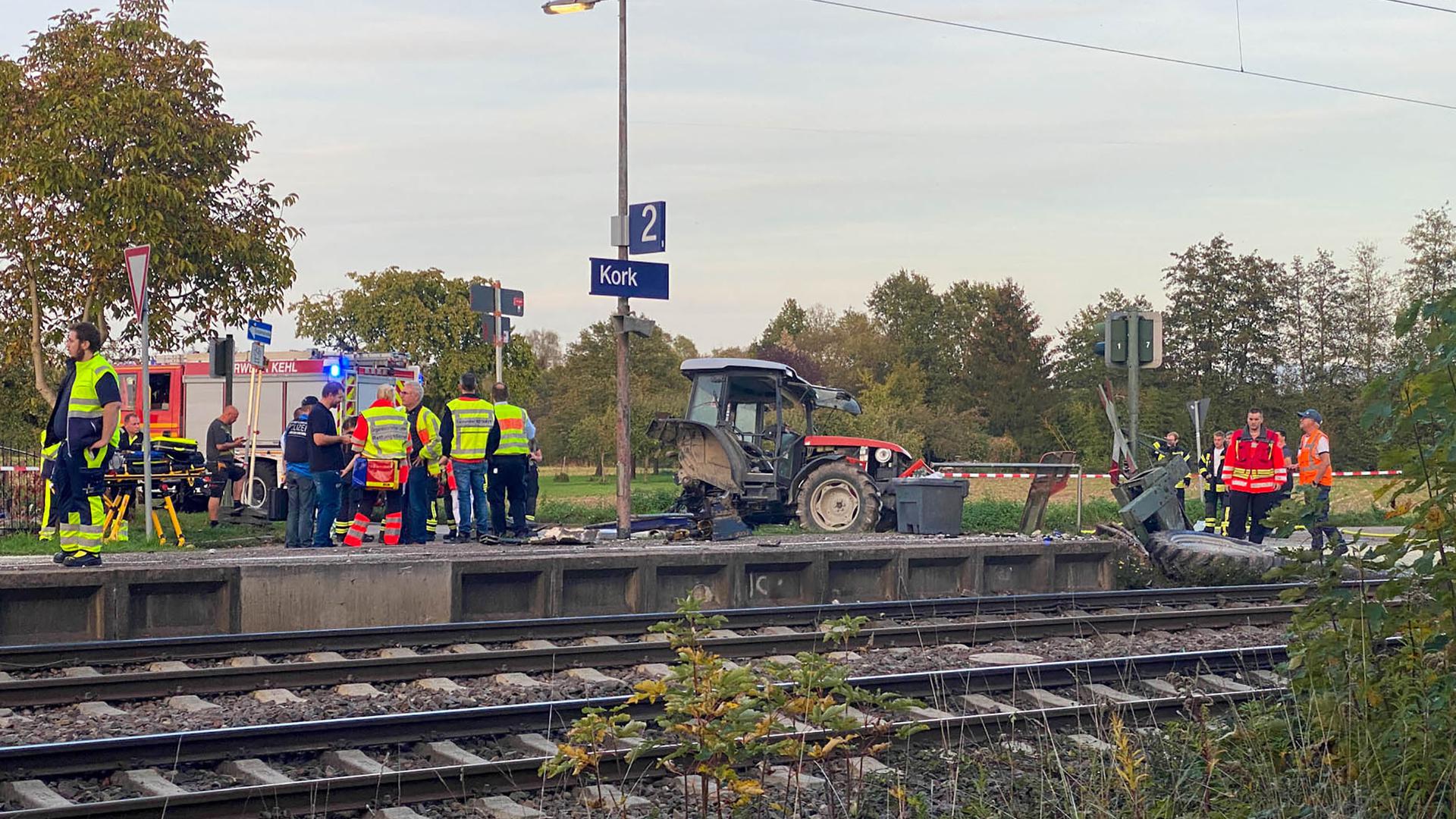 Ein beschädigter Traktor und Rettungskräfte stehen am Bahnhof Kork, einem Stadtteil von Kehl. Laut Polizei ist der Traktor auf dem Bahnübergang liegengeblieben.