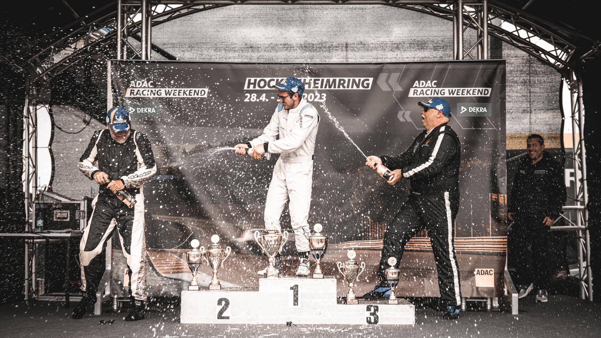 Drei Rennfahrer auf dem Siegerpodest, in der Mitte Yannik Dinger aus Lauf, feiern mit Champagner