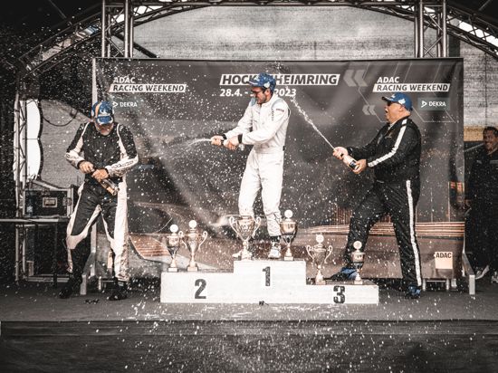 Drei Rennfahrer auf dem Siegerpodest, in der Mitte Yannik Dinger aus Lauf, feiern mit Champagner