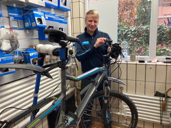 Fahrradmechaniker Patrick Ritmman steht in der Werkstatt an einem Montageständer und arbeitet an einer Schaltung