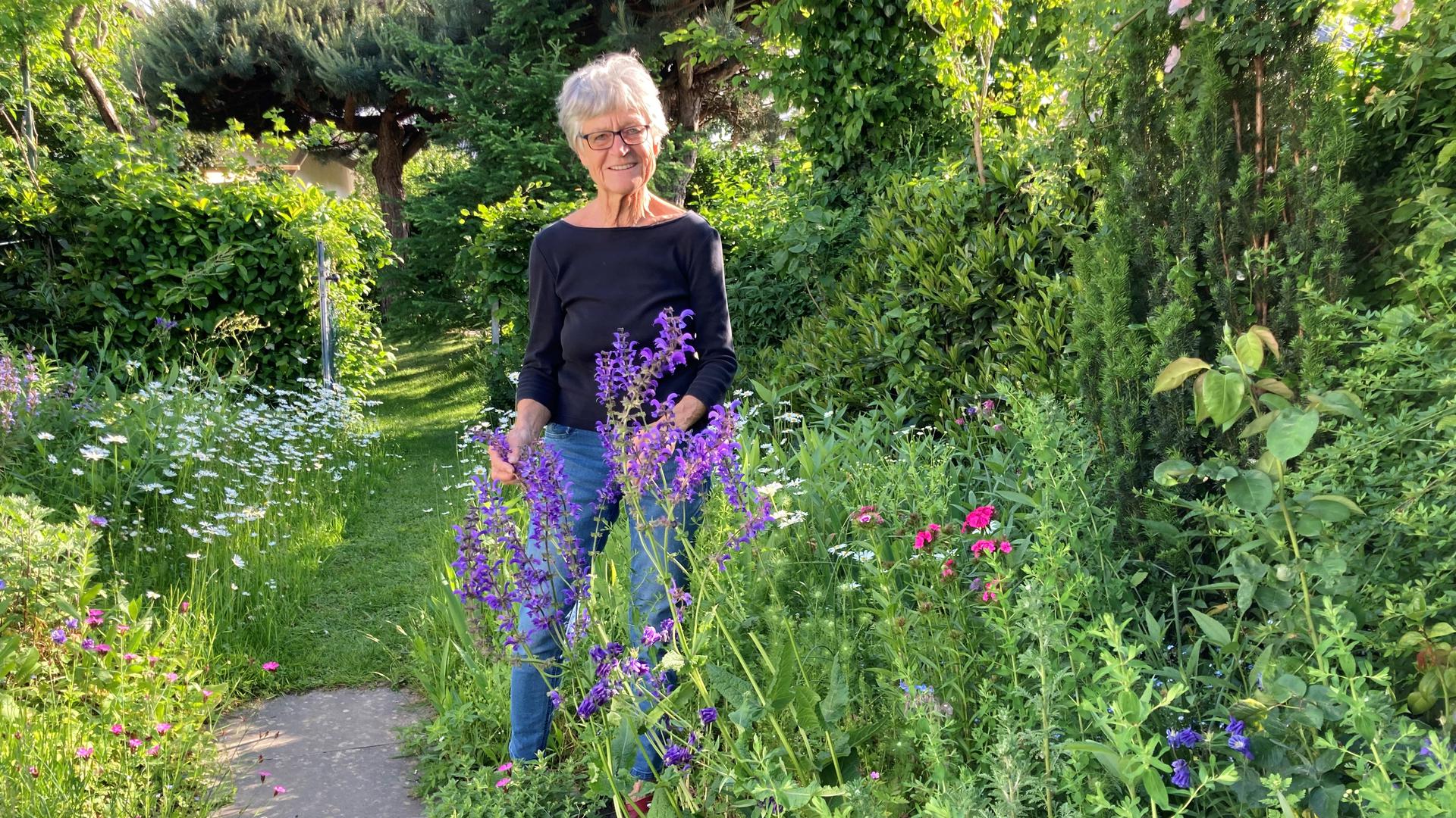 Ulla Rothmund steht in Sasbach bei Achern in ihrem Garten hinter einem blau blühenden Salbei.