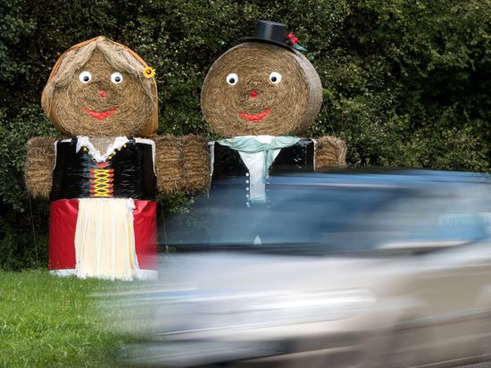 Zwei trachtgeschmückte Strohpuppen stehen in Sasbachwalden (Baden-Württemberg) an der Straße und werben für das Erntedankfest