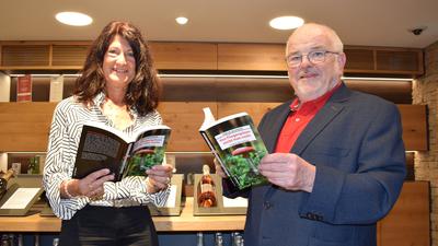 Eine Frau und ein Mann stehen in einer Weinhandlung und halten geöffnete Bücher in den Händen