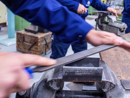 Lehrlinge arbeiten mit der Metallfeile an Schraubstöcken in einer Lehrwerkstatt in Wismar.