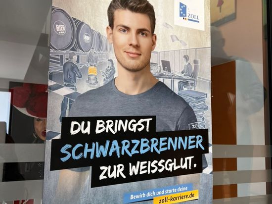 Ein an einer gläsernen Bürotür klebendes Plakat des Zolls zur Mitarbeiter-Werbung zeigt einen junge Mann und die Aufschrift „Du bringst Schwarzbrenner zur Weißglut“. 