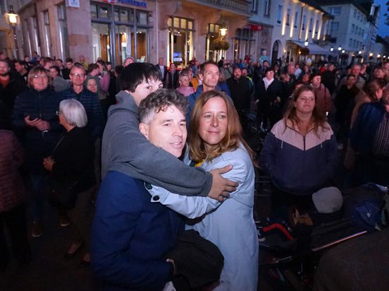 Mann, Frau und Kind umarmen sich vor einer Menschenmenge.